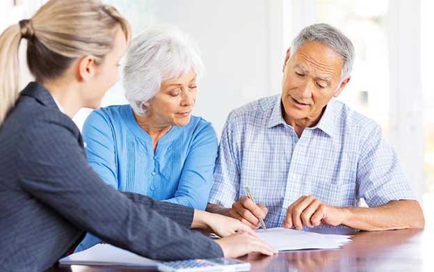 senior couple sitting across from their elder law attorney, reviewing and signing documents