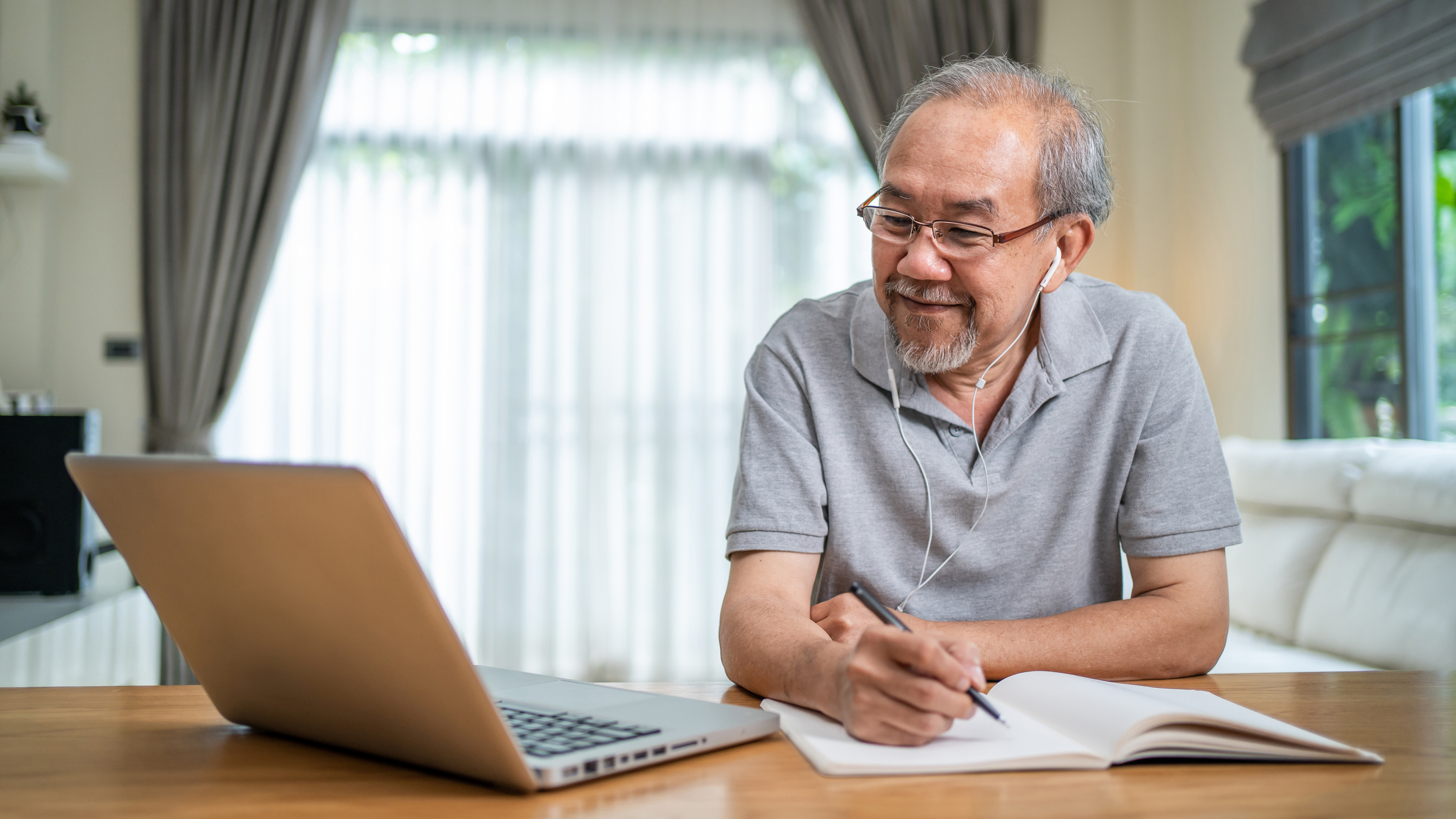 senior man sitting in his kitchen looking at her laptop and taking notes